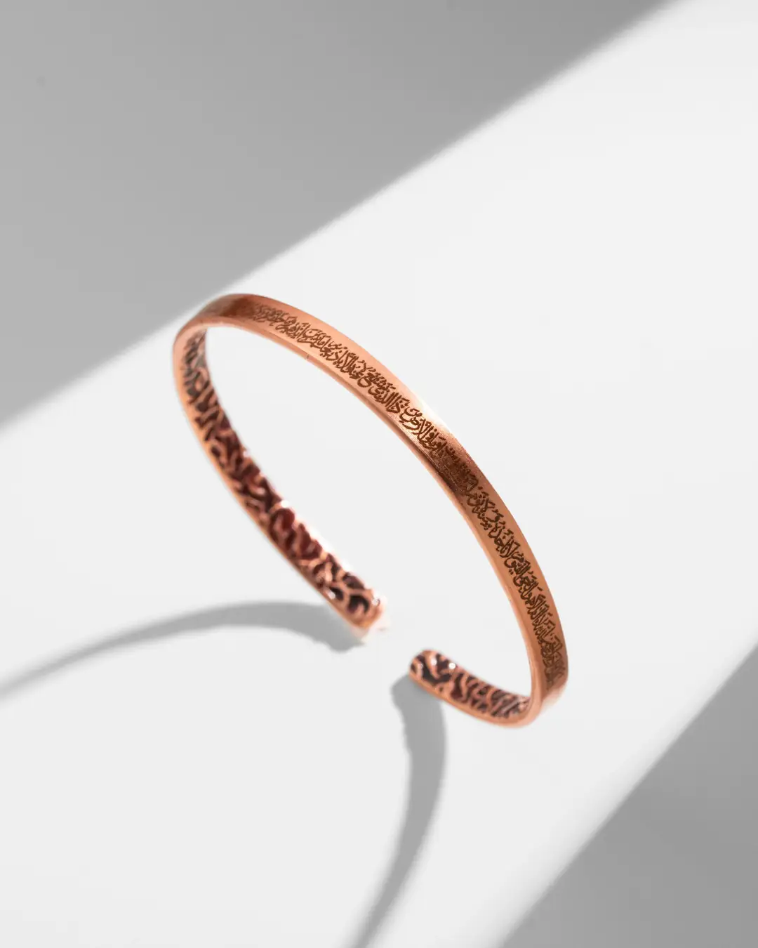 A thin copper bracelet with Ayat al-Kursi inscription on the outside and ivy pattern on the inside.